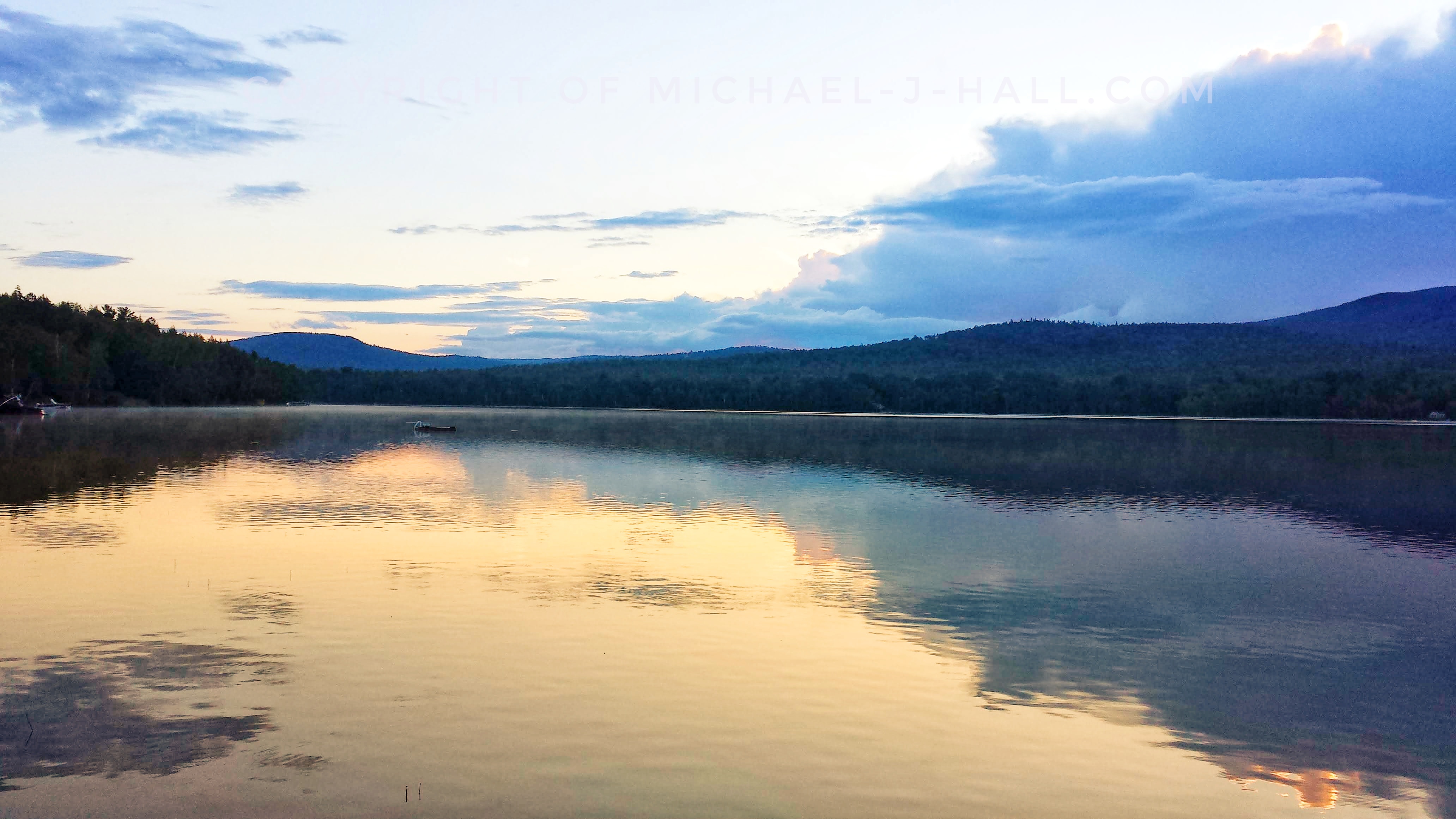 The first gleam of dawn breaks over the dimpled pond surface stretching out toward the distant hills, attempting to awake the forest with its gentle kiss of warm light.